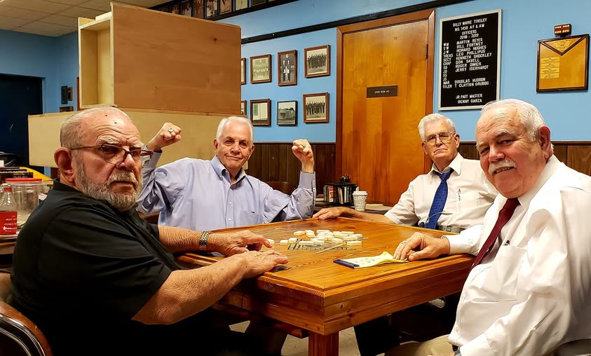 Members around a domino table playing Texas 42